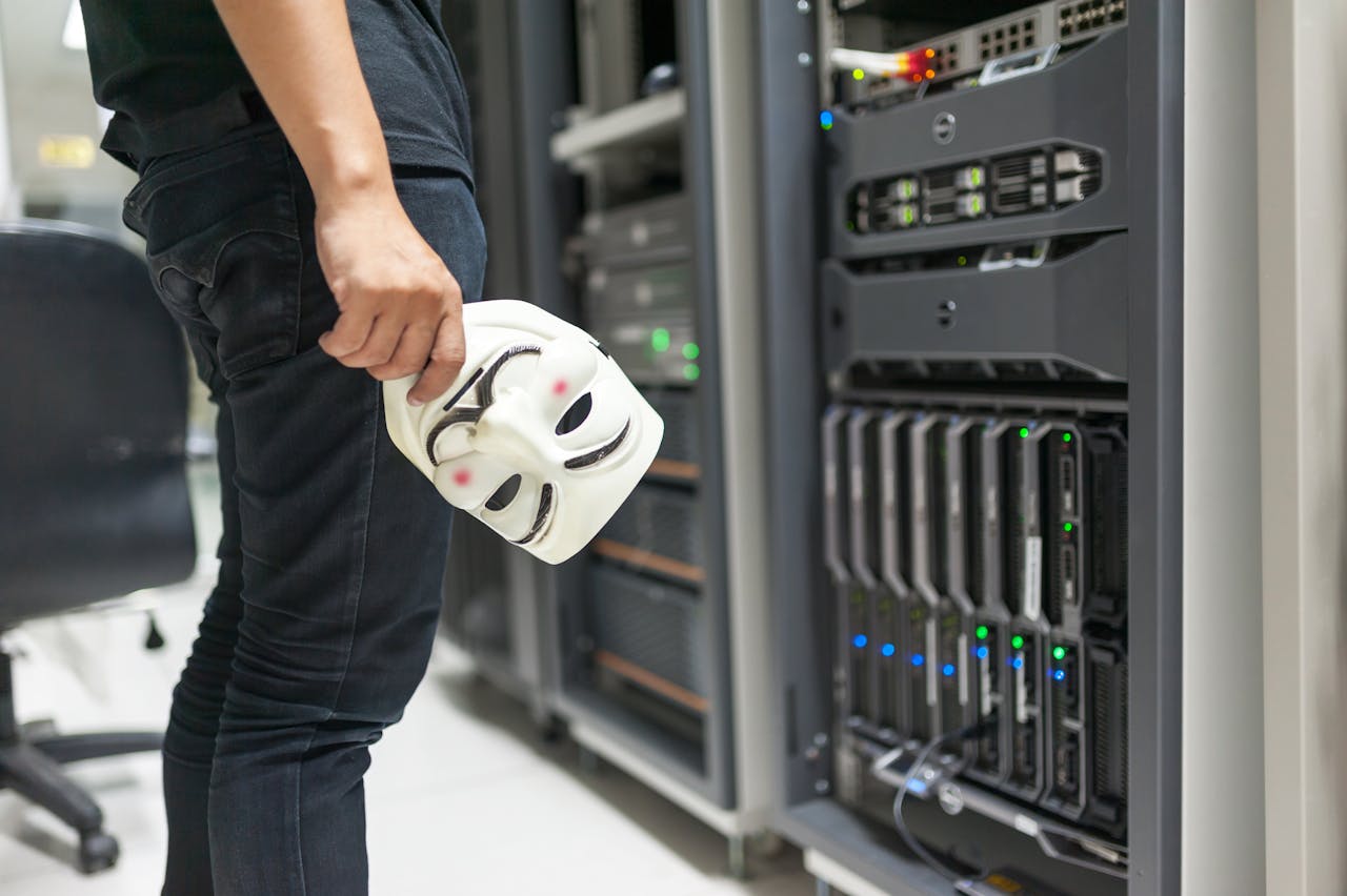 services-02 Person holding anonymous mask near servers, hinting at cybersecurity and hacking themes.